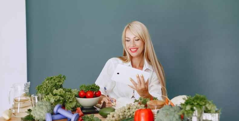 Woman using a tablet surrounded by fresh vegetables at a table, showcasing healthy lifestyle and technology.